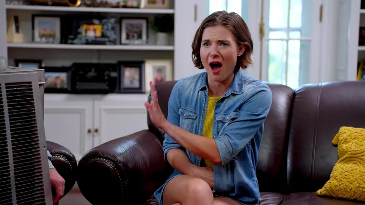 A woman on a leather couch throwing up a hand in alarm