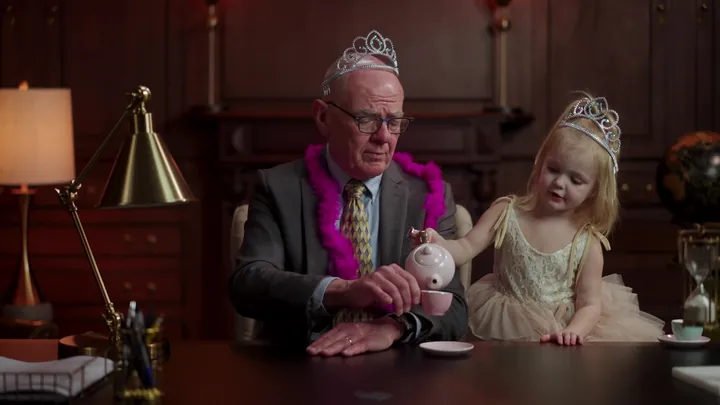 A man in a tiara and feather boa at a tea party with a little girl in a tiara
