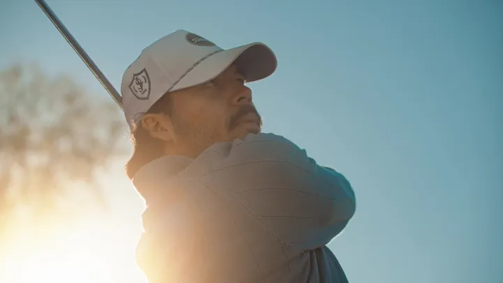 A golfer finishing his swing against a bright sky