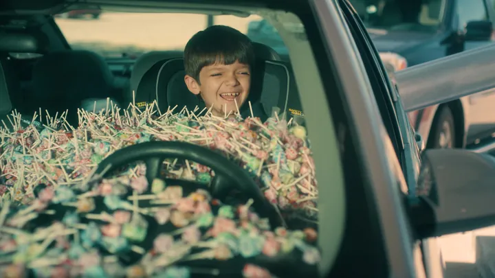 A grinning boy in a car seat, buried in lollipops