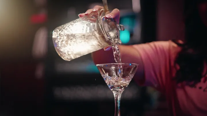A bartender pouring a cocktail into a coupe glass